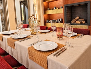 A dining area with tables set for a meal, featuring clear glassware and plates, a decorative golden centerpiece, and a fireplace in the background. - Villa Lenha (Marrakech)