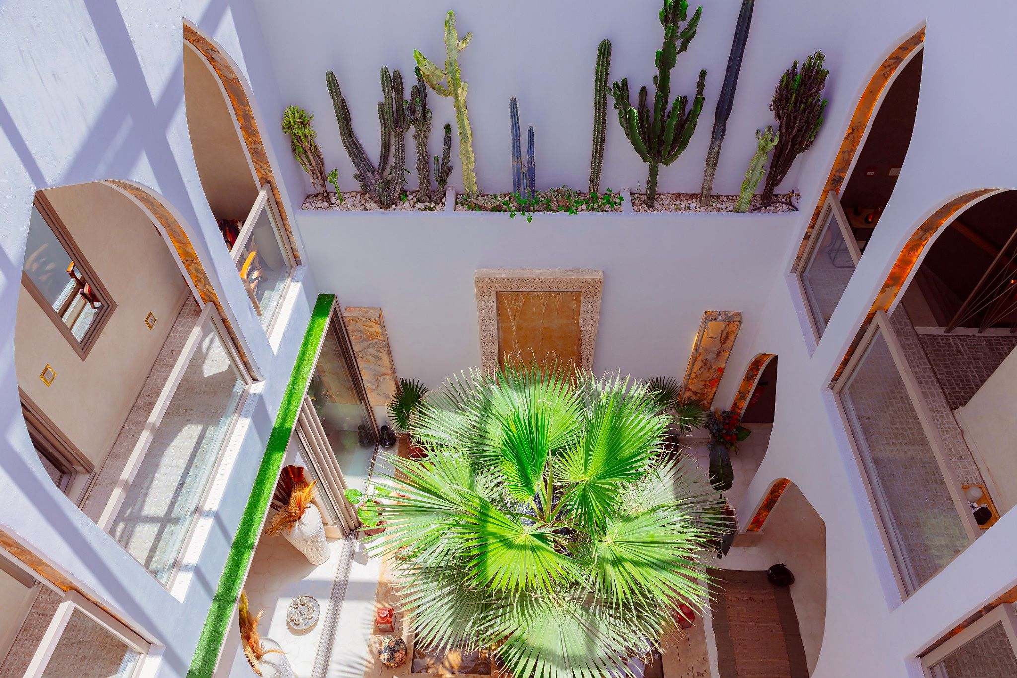 Un atrio de varios niveles con pasarelas arqueadas, una palmera en el centro y diversos cactus en el nivel superior.