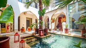 A pool area with a fountain, surrounded by potted plants and red lanterns. - Villa Lenha (Marrakech)