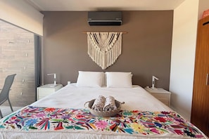 A hotel room with a bed, a wall-mounted air conditioner, a macrame wall hanging, and a colorful embroidered throw. - Beachfront Views Next to the Pier (Puerto Morelos)