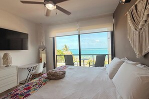A bedroom with a large bed, a desk, a chair, a TV, and a balcony with a view of the ocean. - Beachfront Views Next to the Pier (Puerto Morelos)