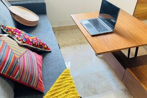 A room with a wooden table, a laptop, a grey sofa, and colorful pillows. - Beachfront Views Next to the Pier (Puerto Morelos)