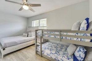 A bedroom with two bunk beds, a ceiling fan, a window with blinds, and a wooden floor.