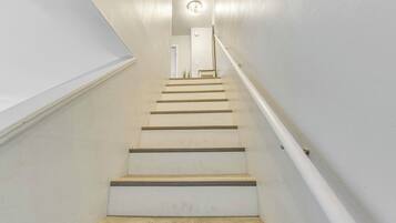 Un escalier aux murs blancs, doté d’une rampe, qui mène à une porte située en haut.