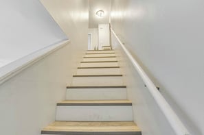 A staircase with white walls and a handrail, leading to a door at the top.
