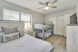 A bedroom with a bed, bunk beds, a desk, a lamp, and a ceiling fan.