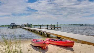 A pier extending into calm waters with kayaks on the sand.