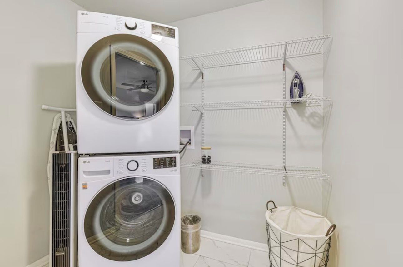 A laundry area with stacked washers and dryers, a metal rack, and a trash can.