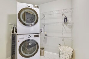 A laundry area with stacked washers and dryers, a metal rack, and a trash can.