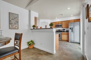 A modern kitchen with a central island, wooden cabinets, stainless steel appliances, and a dining area with a chair and table. - GEM/3BD/flex office space/sleeps 6/private 2 car garage/20 min strip & airport, (Las Vegas)
