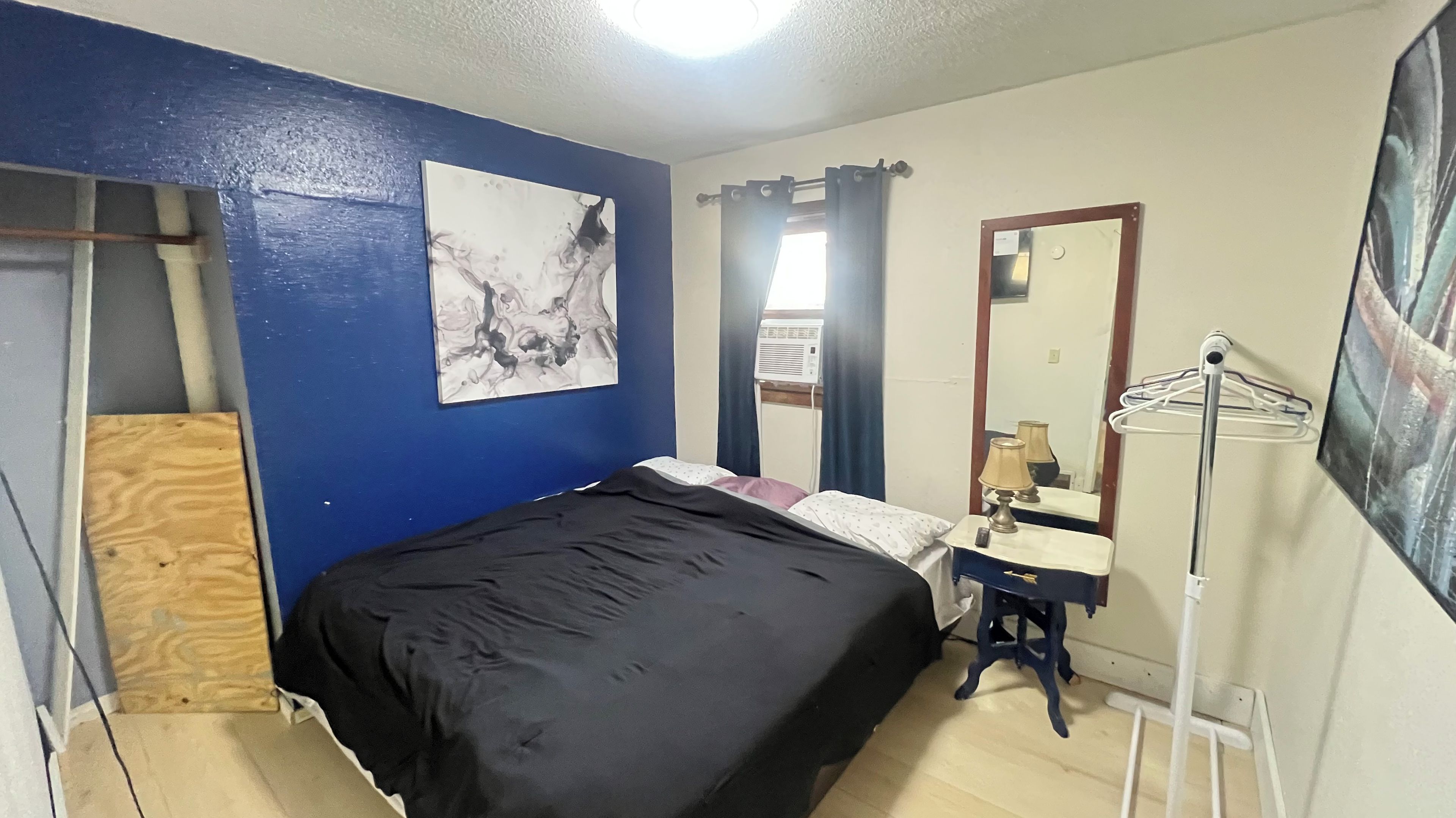 Une chambre à coucher avec un lit, une table de chevet avec une lampe, un miroir et un étendoir fixé au mur.