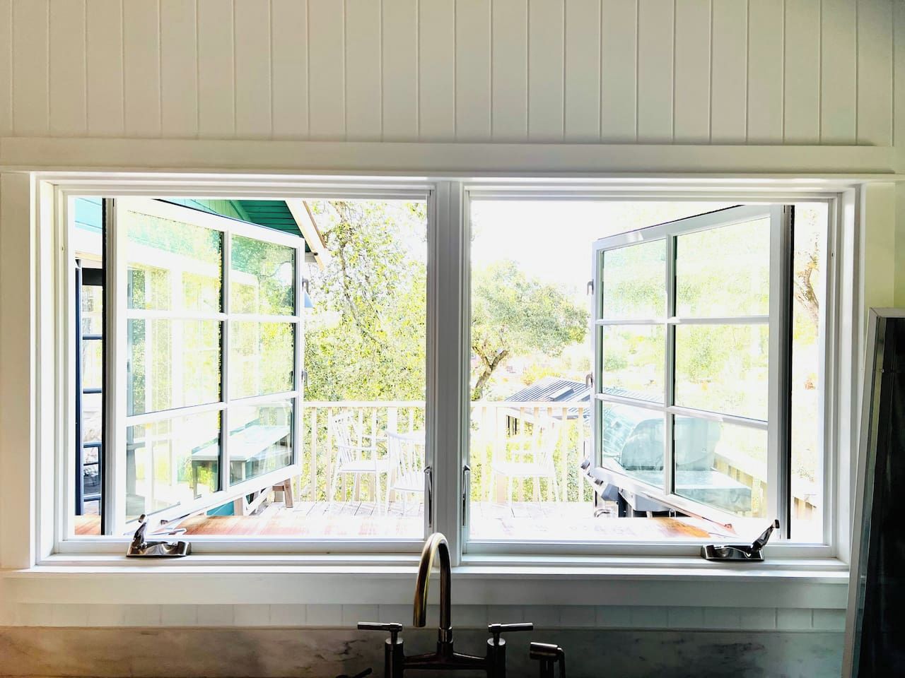 A kitchen with a double window, a sink, and a view of an outdoor deck.