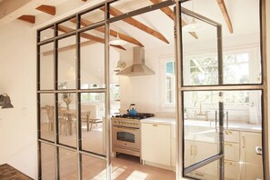 A kitchen with a stove, cabinets, and a dining area visible through glass partitions. - Sonoma Winemakers Cottage (Sonoma)