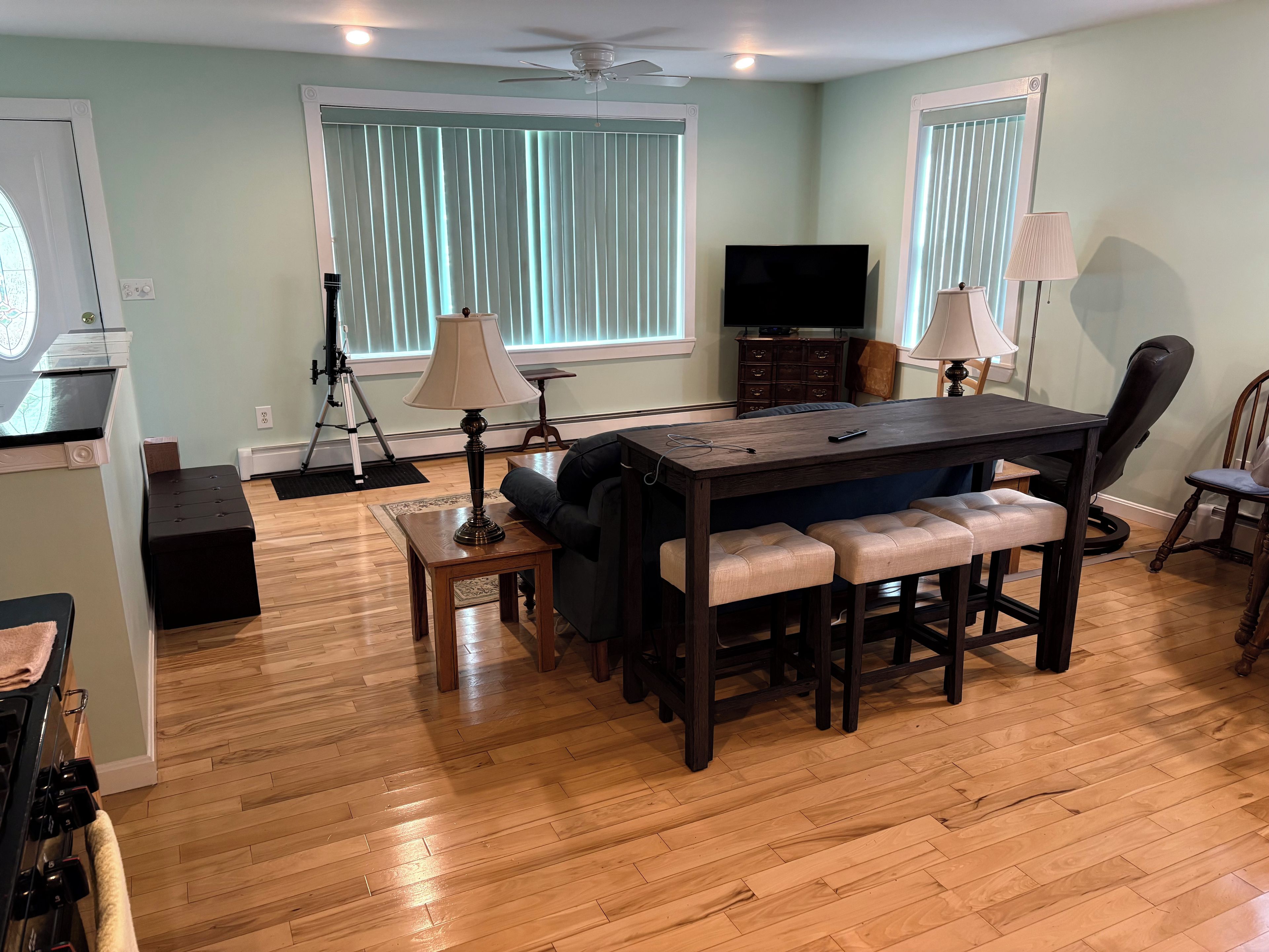 Un salon moderne avec un plancher en bois, une table à manger en bois foncé dotée de bancs rembourrés, un canapé, un téléviseur et un ventilateur de plafond.