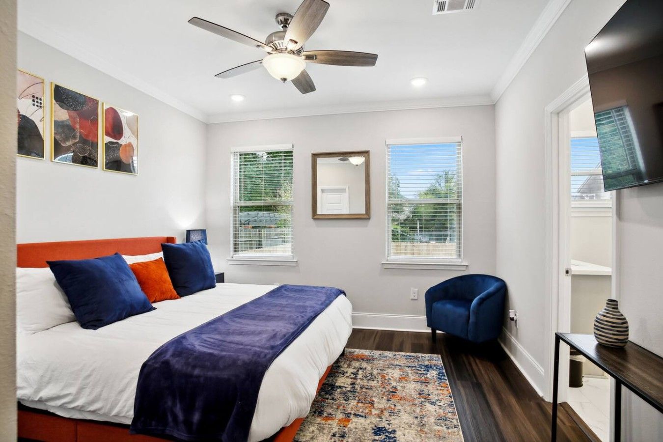 A bedroom with a bed, a ceiling fan, a TV, and a window.