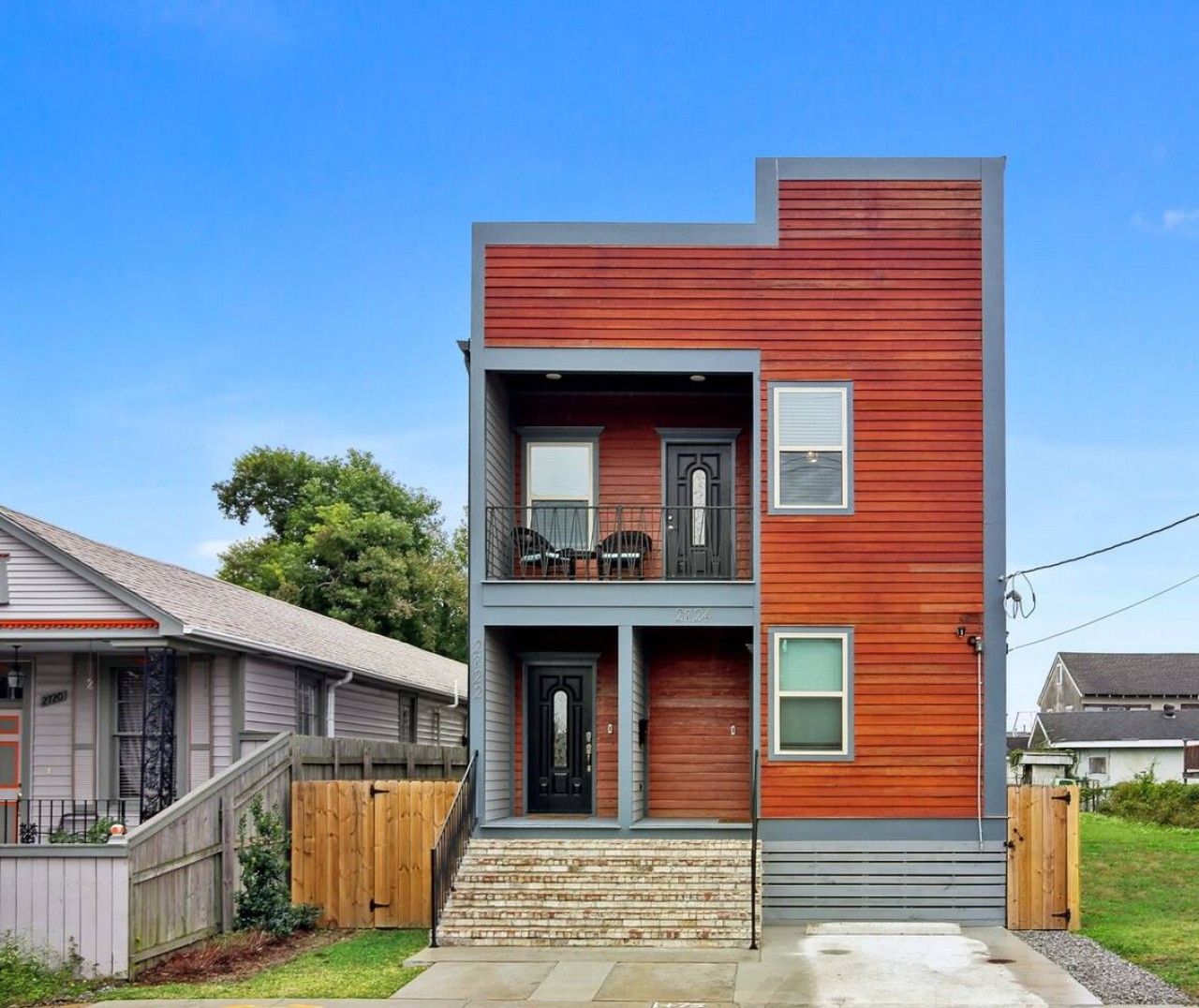 A two-story building with a wooden facade, a balcony on the upper floor, and a front door with a small porch.
