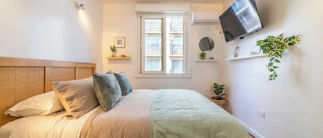 A bedroom with a bed, a television mounted on the wall, and a window with blinds.