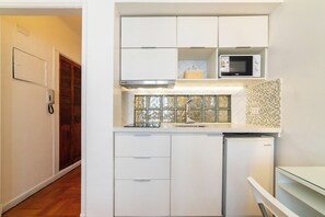 A compact kitchen with white cabinets, a microwave, and a refrigerator. - Chic Urban Home in Providencia (Providencia)