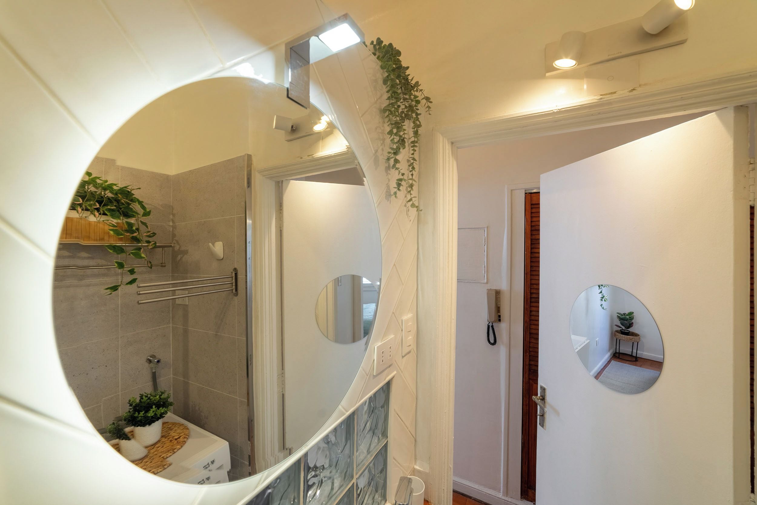 A bathroom with a shower, a toilet, a sink, and a mirror. There are plants and a towel rack.