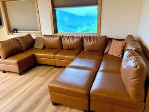 A sectional sofa with a view of a mountainous landscape through a large window. - Appalachian Mountain Retreat (Boone)