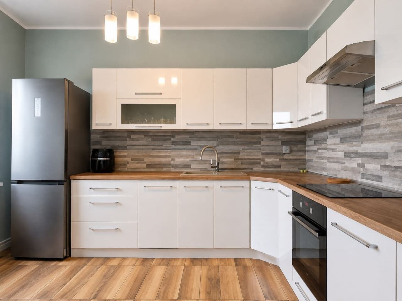 Cocina moderna con armarios blancos, un refrigerador de acero inoxidable, horno empotrado y encimera de madera.