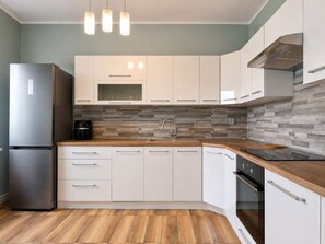 Eine moderne Küche mit weißen Schränken, einem Edelstahl-Kühlschrank, einem Einbauofen und einer Holz Arbeitsplatte.