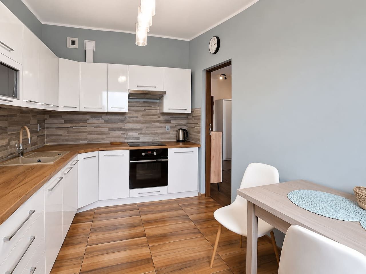 A modern kitchen with white cabinets, a built-in oven, and a wooden countertop.