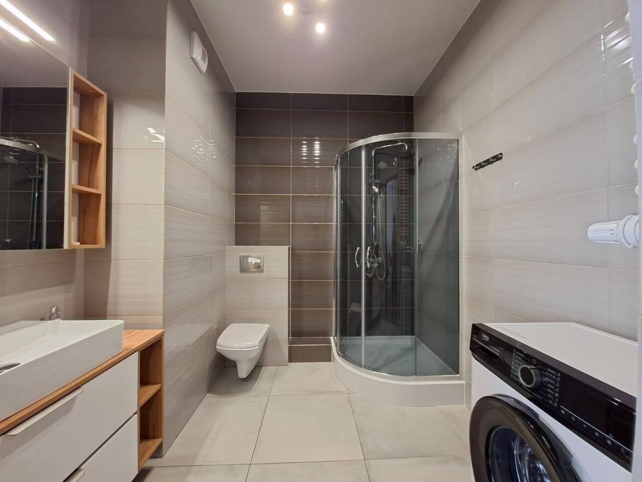 Un baño moderno con cabina de ducha de vidrio, inodoro y lavadora.