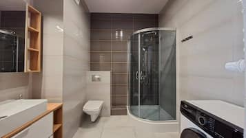 Un baño moderno con cabina de ducha de vidrio, inodoro y lavadora.