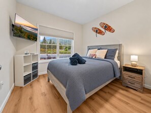 Ein Schlafzimmer mit einem Bett, einem an der Wand befestigten Fernseher, einem Fenster mit Blick und einem Nachttisch mit Lampe.