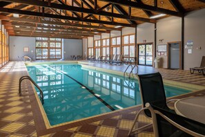 Ein Innenpool mit klarem Wasser, Holzbalken an der Decke und sonnendurchfluteten Fenstern.