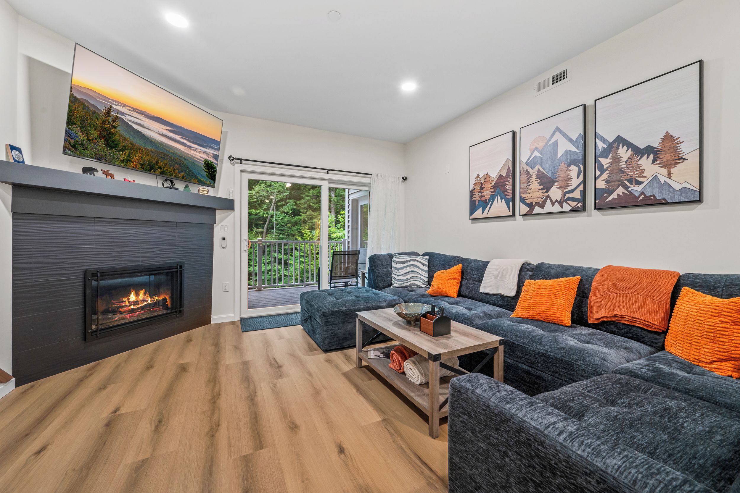 A modern living room with a fireplace, a sofa set, and a large window overlooking a deck.