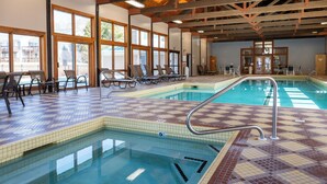 Una piscina interior con pisos y paredes de azulejos, iluminada por grandes ventanales, equipada con sillones y mesas.