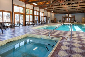An indoor swimming pool with tiled floors and walls, sunlit by large windows, and equipped with lounge chairs and tables. - New 2026 Build · 3 Min to Loon · Movie Room · Pool & Hot Tub · Sleeps 20 (Lincoln)