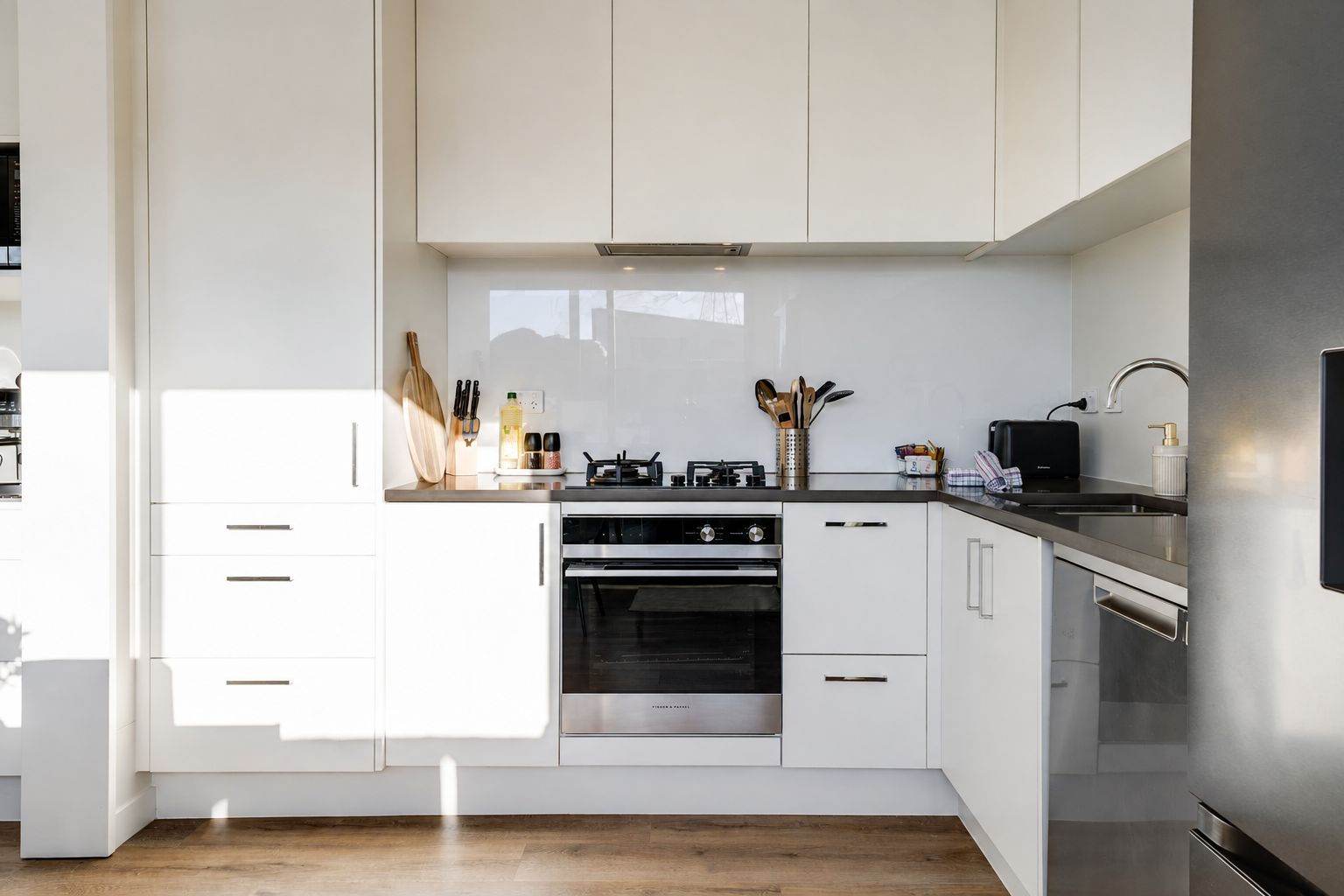 A modern kitchen with white cabinetry, stainless steel appliances, and a wooden floor.