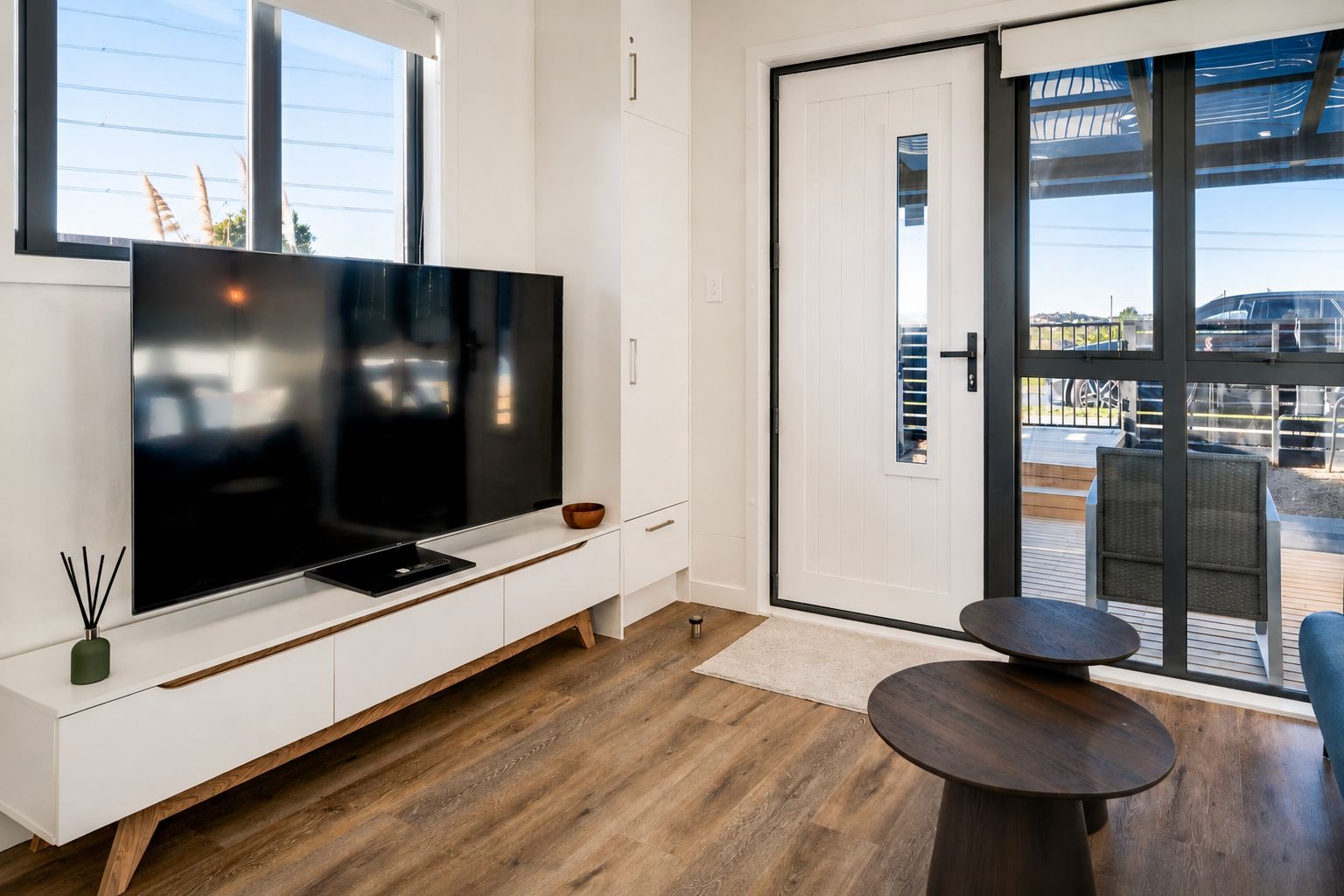 Un salon moderne doté d’un téléviseur à écran plat, de planchers en bois, d’une petite table et d’une porte-fenêtre coulissante donnant sur un espace extérieur.
