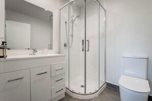 Un baño moderno con ducha envuelta en vidrio, un tocador blanco con cajones y un inodoro.
