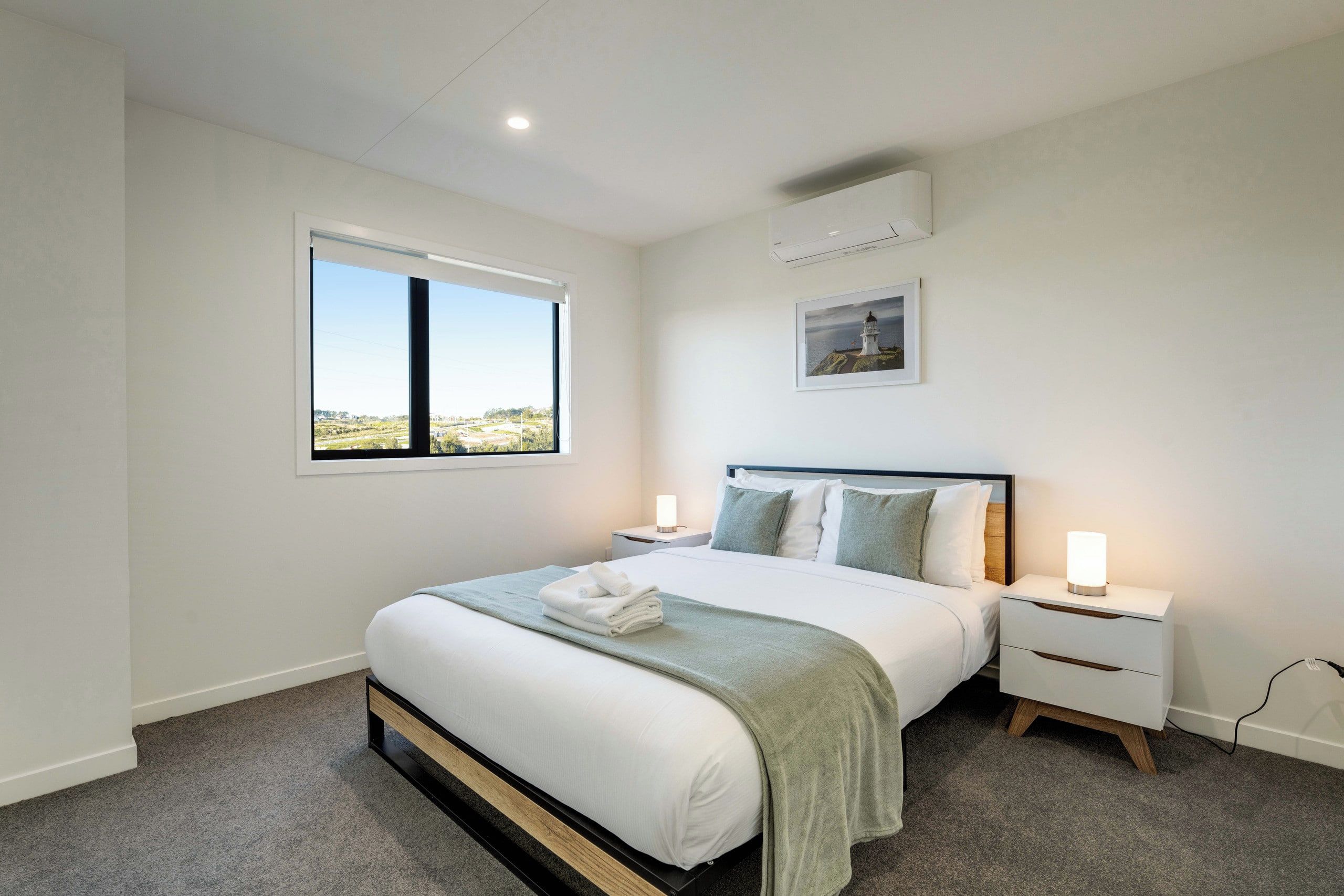 Une chambre à coucher comprenant un lit, des tables de chevet, une fenêtre, un appareil de climatisation et un tableau accroché au mur.