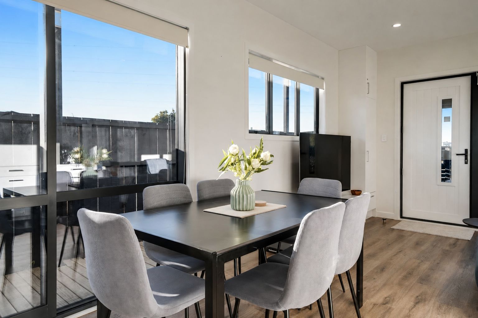A modern dining area with a glass partition, a dark wooden table, and grey upholstered chairs.