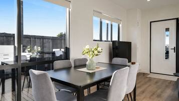 A modern dining area with a glass partition, a dark wooden table, and grey upholstered chairs.