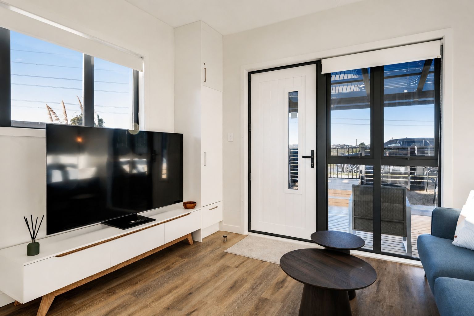 A modern living room with a flat-screen TV, a sofa, a coffee table, and a sliding glass door leading to an outdoor area.