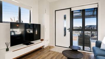 A modern living room with a flat-screen TV, a sofa, a coffee table, and a sliding glass door leading to an outdoor area.