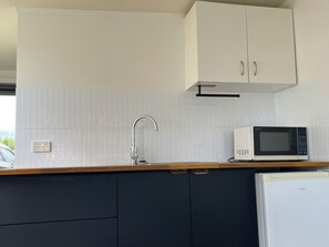 A kitchen with white cabinets, a microwave, and a refrigerator. - Pukehina beach house: Estuary views + Outdoor bath (Pukehina)