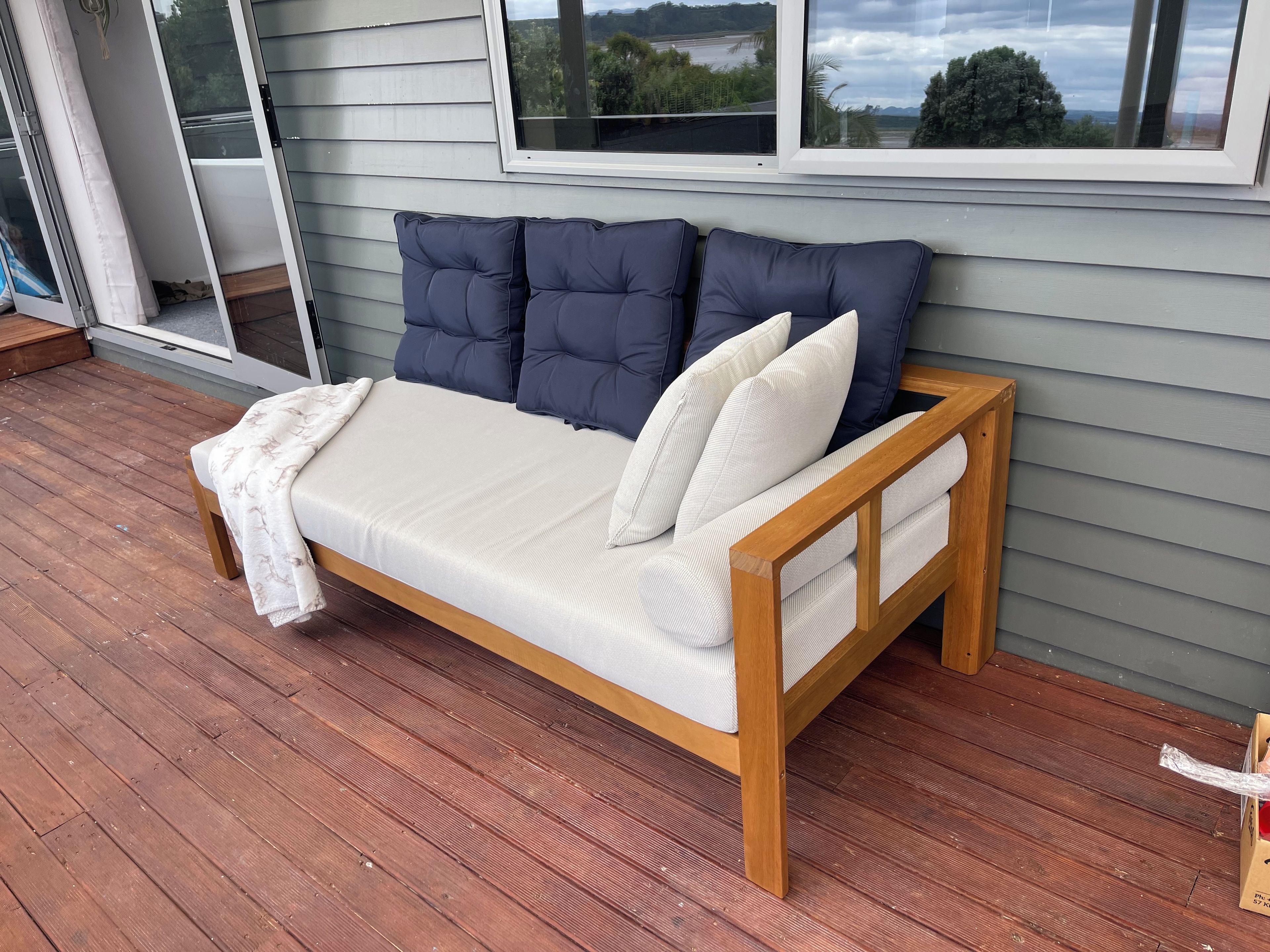 A wooden bench with cushions and a blanket, positioned on a wooden deck.
