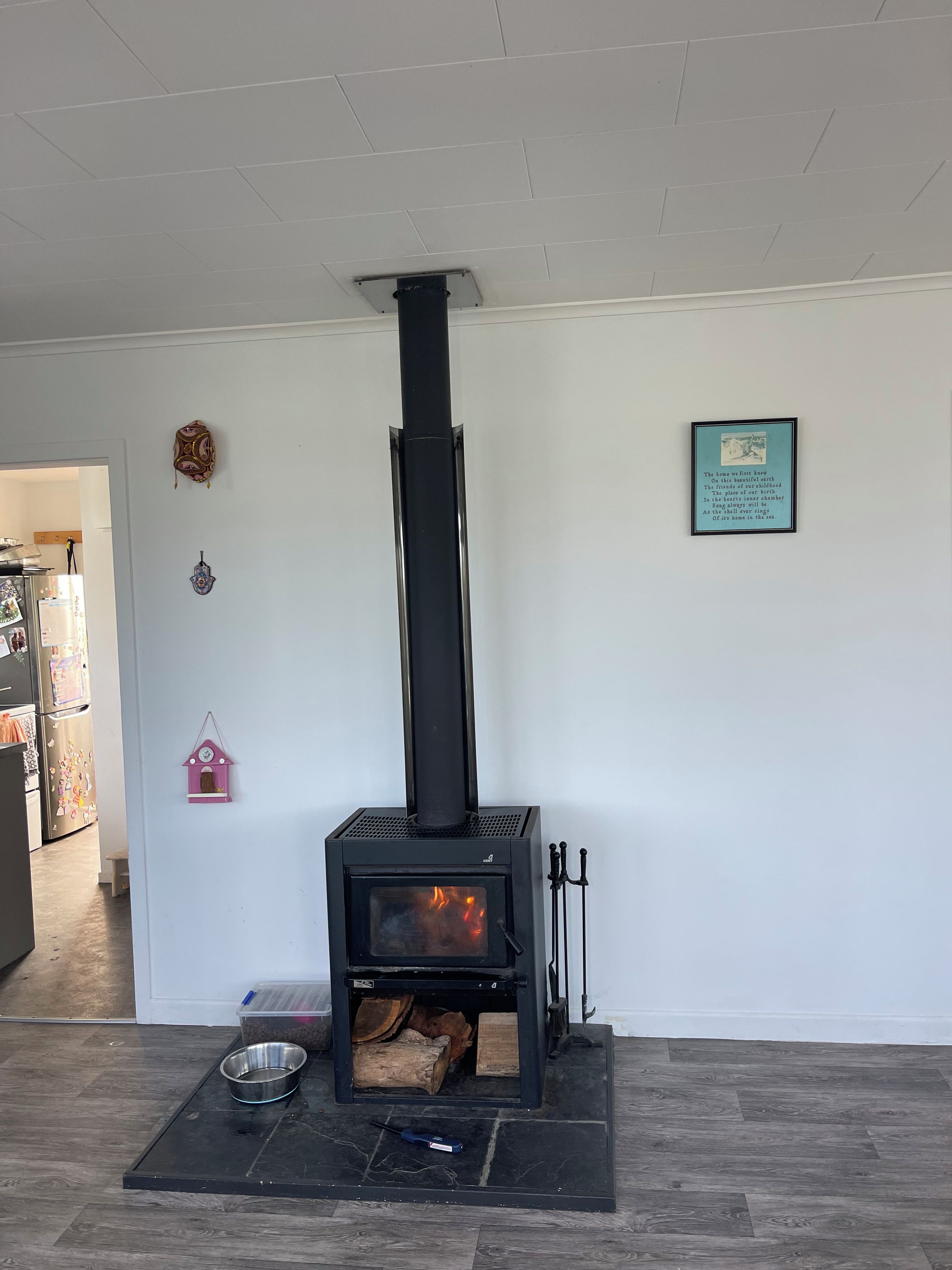 A modern living room with a black wood-burning stove, a framed poem on the wall, and a small pink birdhouse decoration.