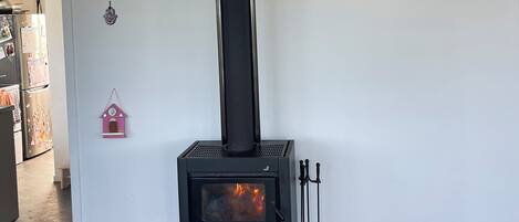 A modern living room with a black wood-burning stove, a framed poem on the wall, and a small pink birdhouse decoration.