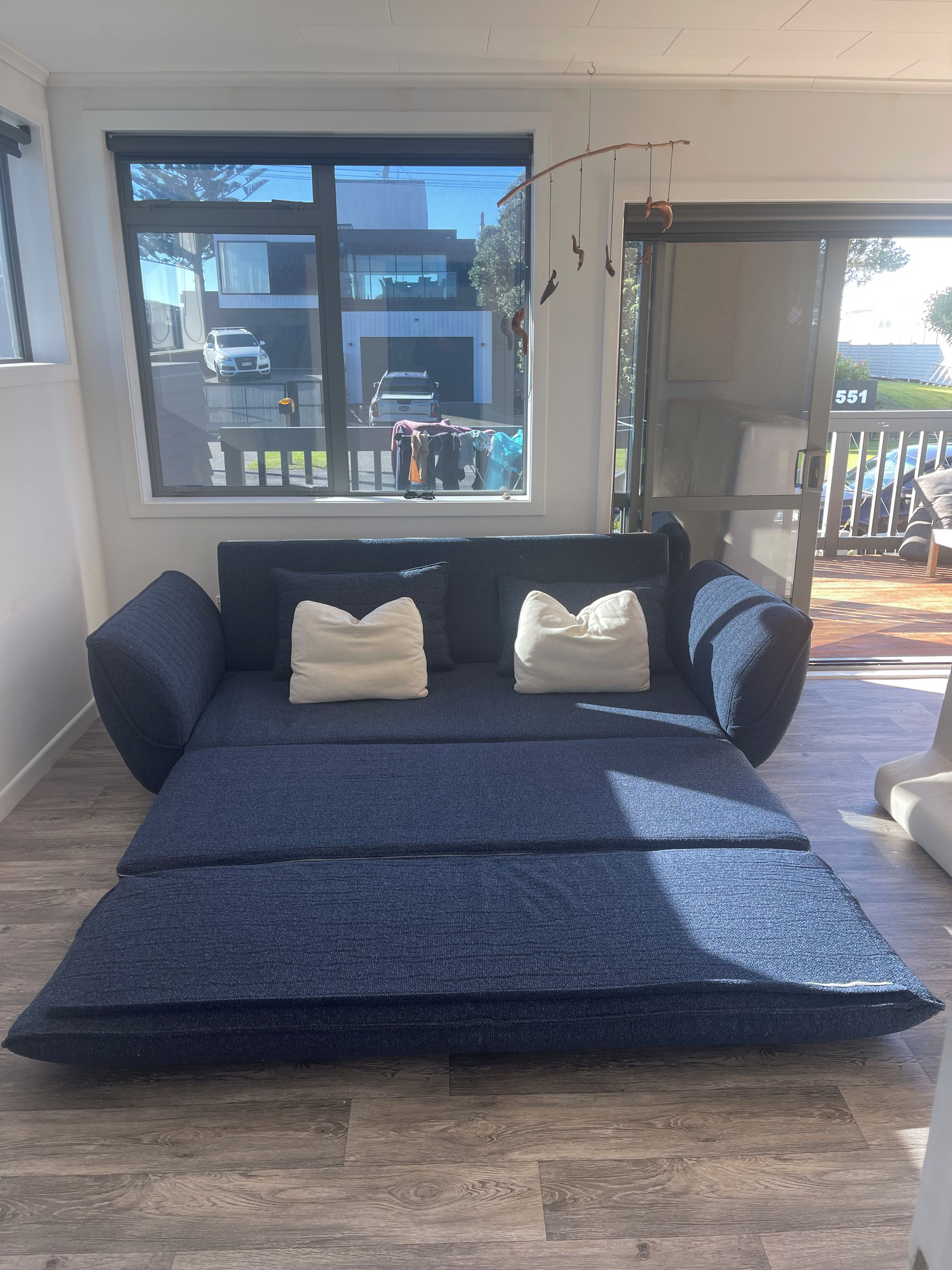 A room with a large window, a sofa with cushions, and a view of a parking area.
