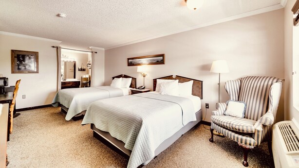 A hotel room with two beds, a chair, a desk, a mirror, and a lamp. - Deerfield Inn - Two Queen Beds - Handicapped (Hayesville)
