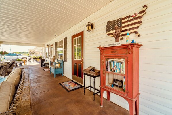 A covered porch with a red bookcase, a wicker sofa, and a wall-mounted American flag decoration.