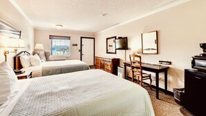 A hotel room with two beds, a desk, a television, and a window with a view. - Deerfield Inn - Two Queen Beds - Handicapped (Hayesville)